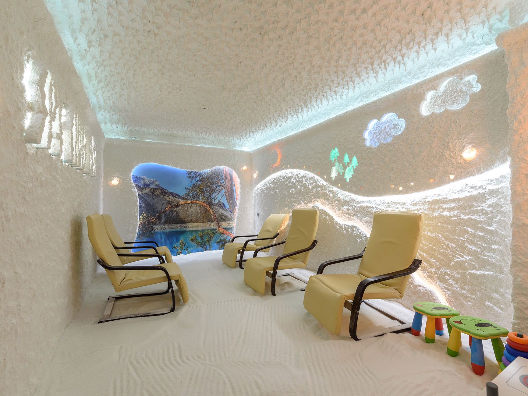 A salt room with loungers, children’s stools and a backlit salt wall